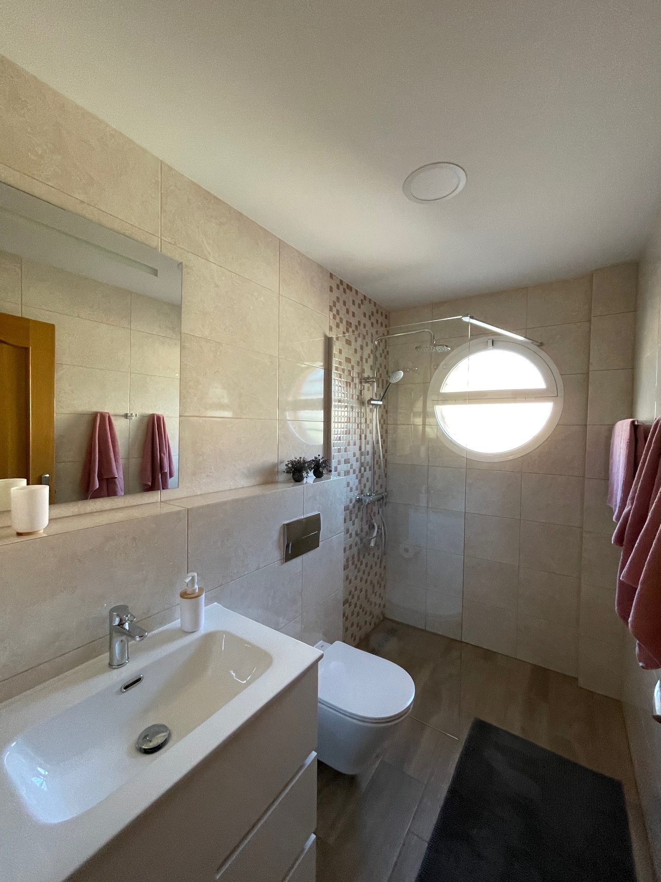 Helles Bad mit Dusche, Waschbecken und rundem Fenster