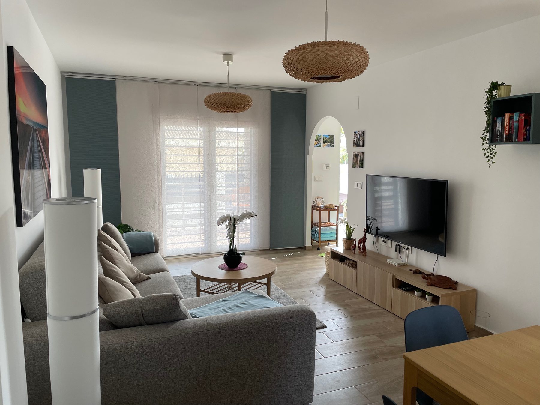 Wohnzimmer mit Sofa, TV und hellem Durchgang